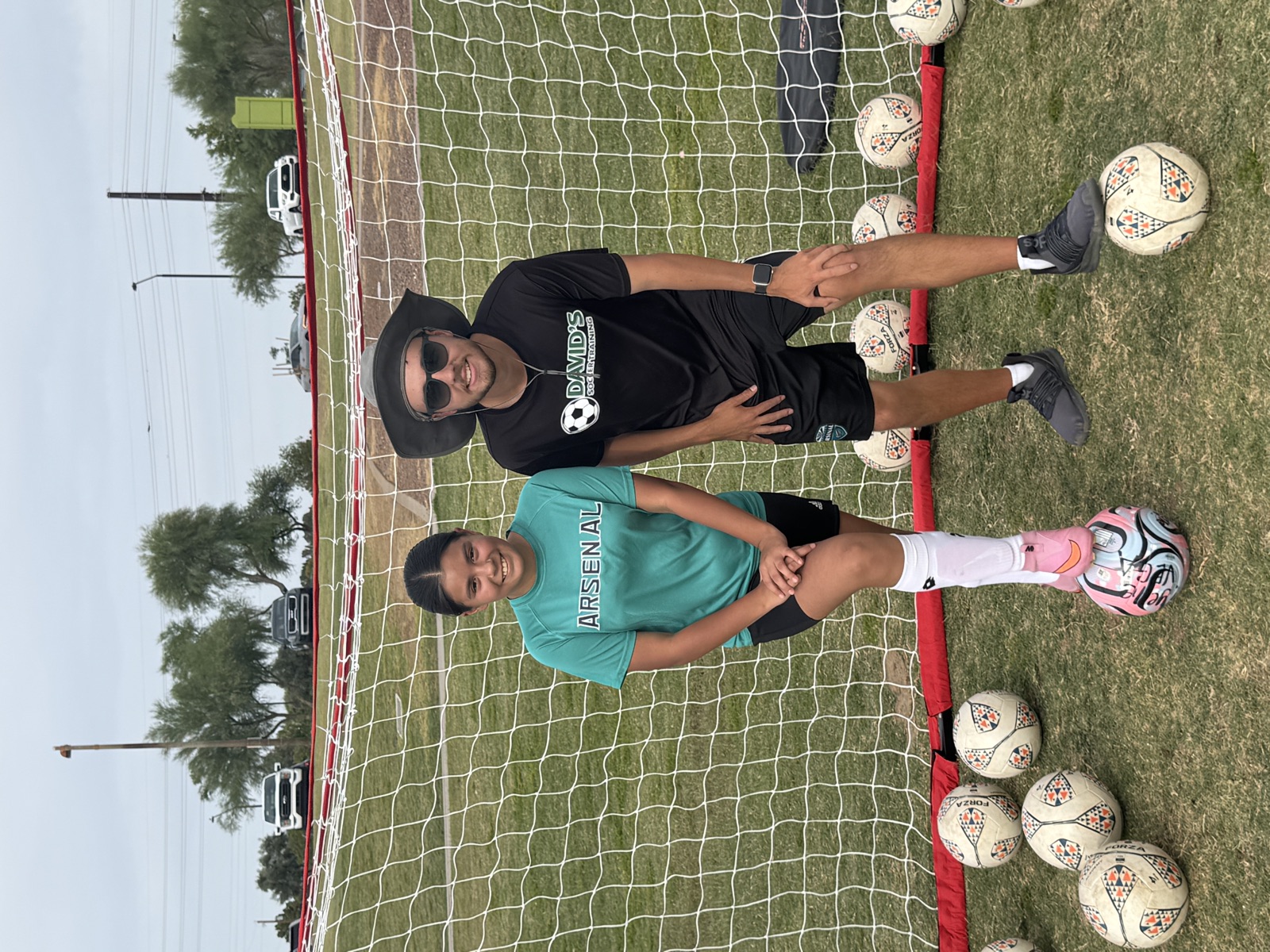 Coach David Fales with a youth player in an Arsenal jersey resting her foot on a ball during a finishing drill.